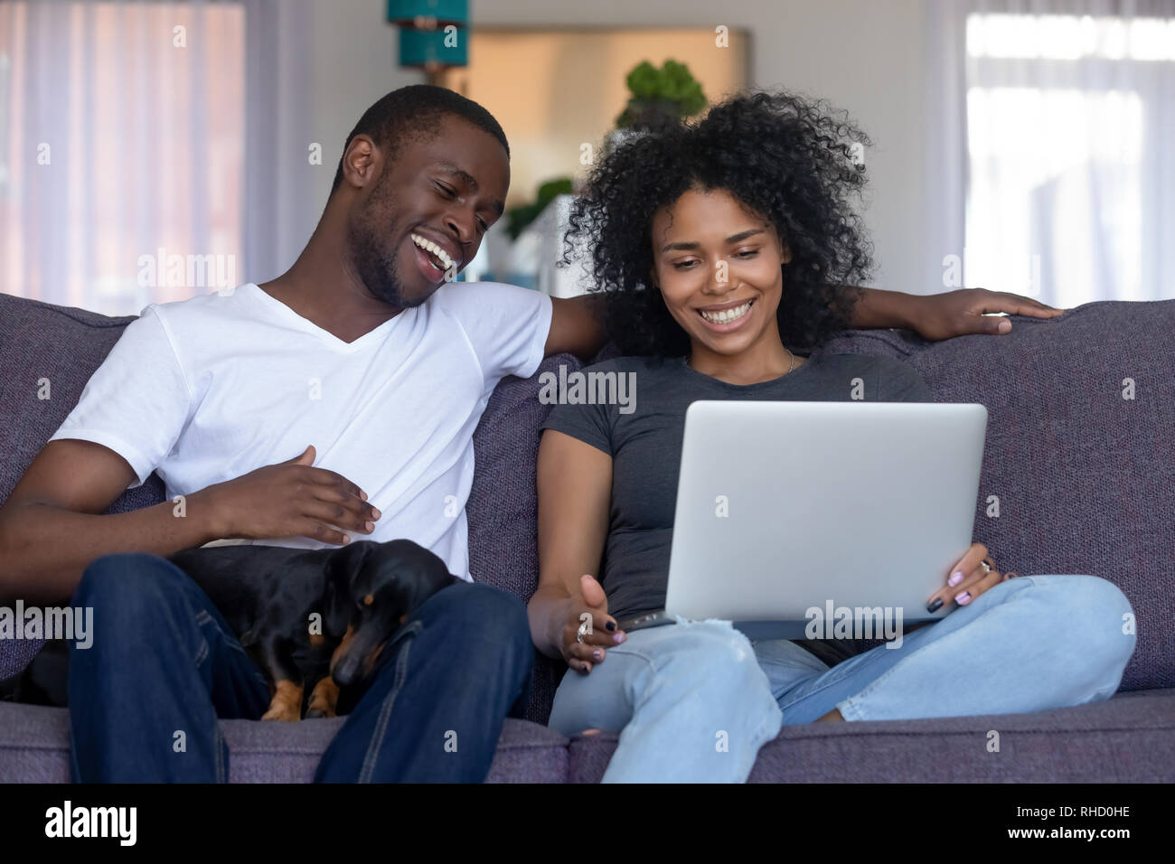 Smiling african couple laughing en utilisant ordinateur avec chien à la maison Banque D'Images