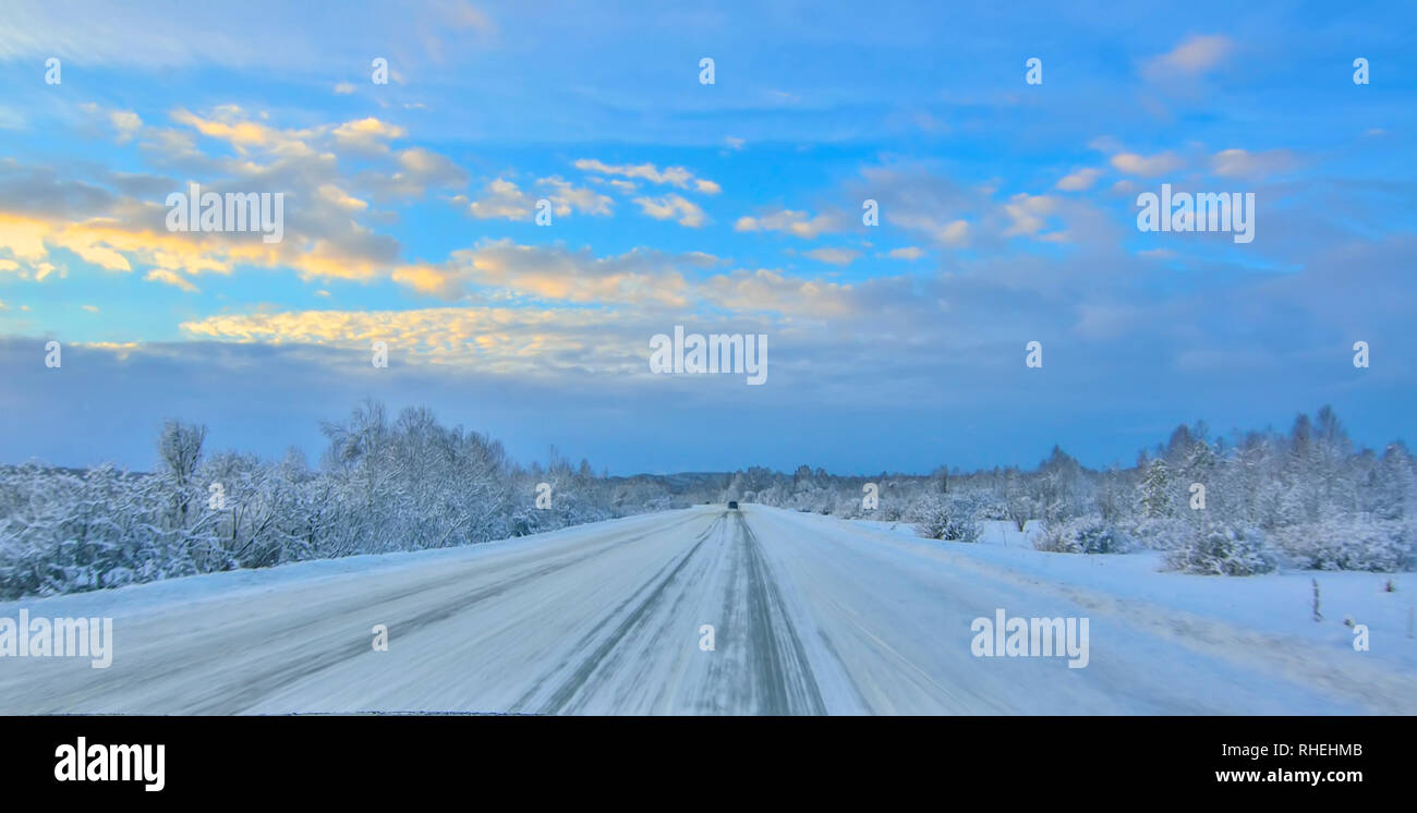 Hiver neige sinueuse route conduisant à travers une vallée de montagne, paysage de forêts couvertes, floue à partir de la haute vitesse. Crépuscule du soir, de l'or Banque D'Images