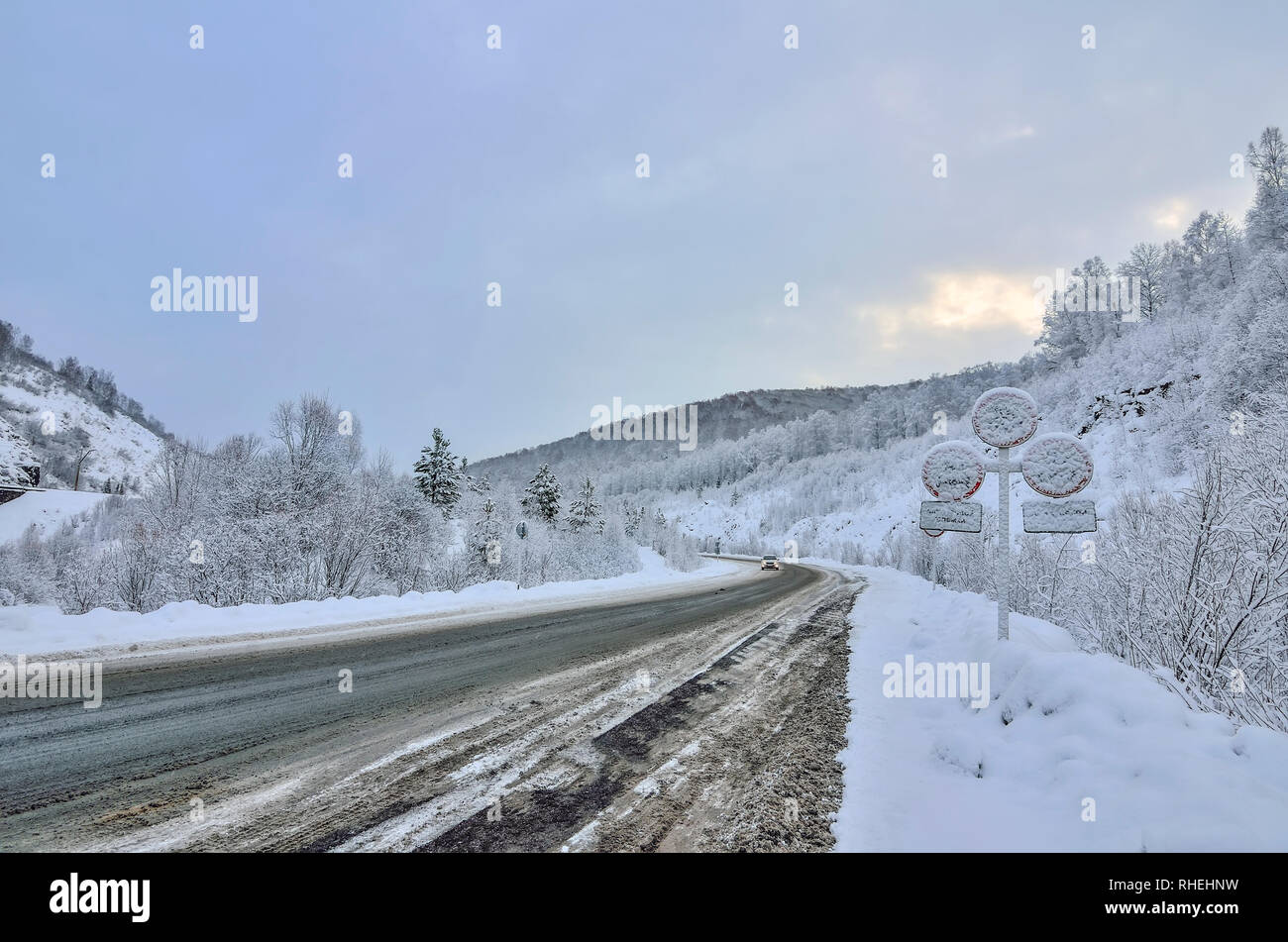 Liquidation d'hiver montagne enneigée route nationale qui mène à travers un paysage de montagne. Au crépuscule, les signaux routiers couverts de neige après une chute de neige - la con Banque D'Images