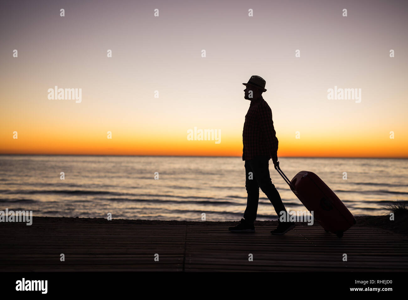 Vacances, l'été et travel concept - jeune homme d'ossature avec valise au coucher du soleil près de la mer Banque D'Images