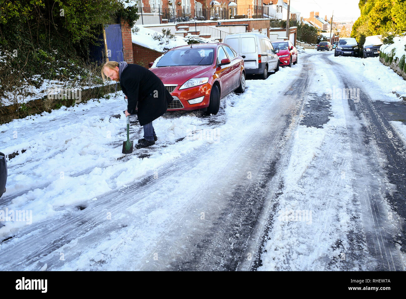 Un homme efface la neige pour essayer gratuitement sa voiture, ce qui est par la neige sur une colline menant au sommet de l'hôtel Westbury White Horse (Wiltshire). Banque D'Images