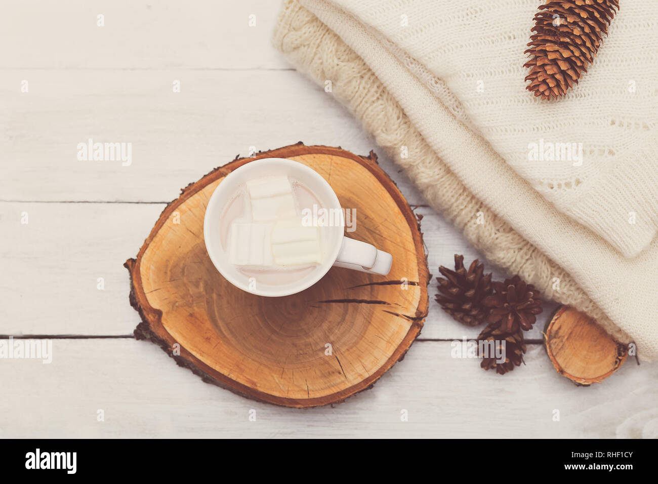 Tasse avec du chocolat chaud et des guimauves, une rangée de cônes et une pile de choses tricotées sur un fond de bois blanc Banque D'Images