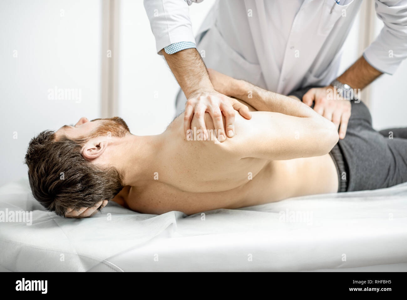 Physiothérapeute senior professionnel faire le traitement manuel d'un homme dans le cabinet de clinique de réhabilitation Banque D'Images