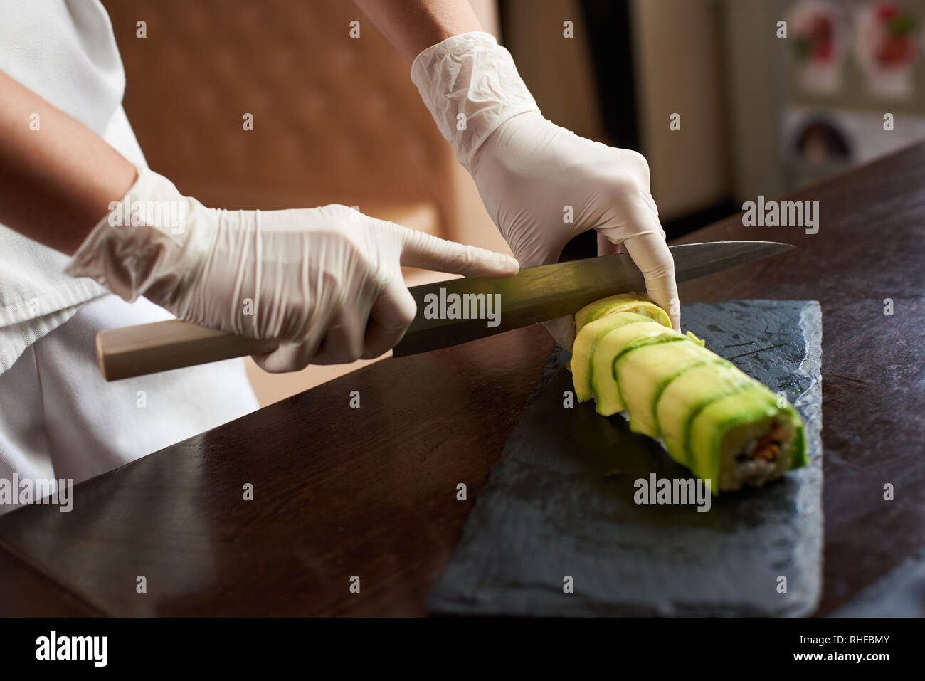 Vue rapprochée du processus de préparation des sushis. Rouleau Coupe Chef est sur la plaque en pierre noire Banque D'Images