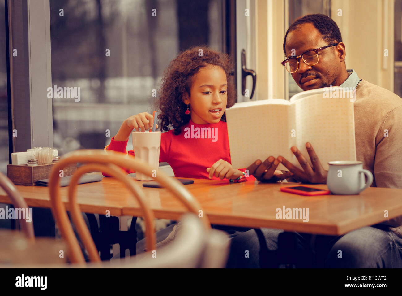Fille d'alcool milkshake et écouter son père reading book Banque D'Images
