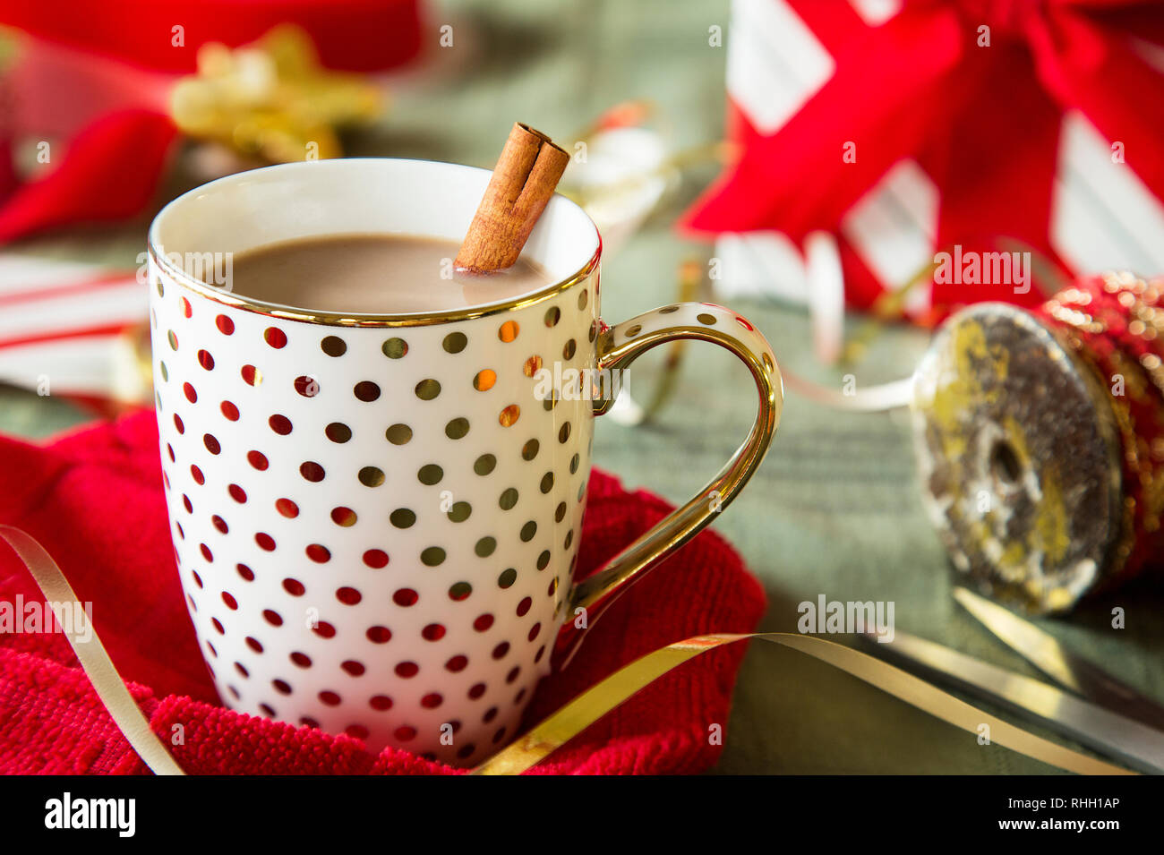 Polka Dot or mug de chocolat chaud avec le bâton de cannelle entre les vacances de Noël, le rouge et le blanc du papier d'emballage et ruban sur la surface verte. Banque D'Images
