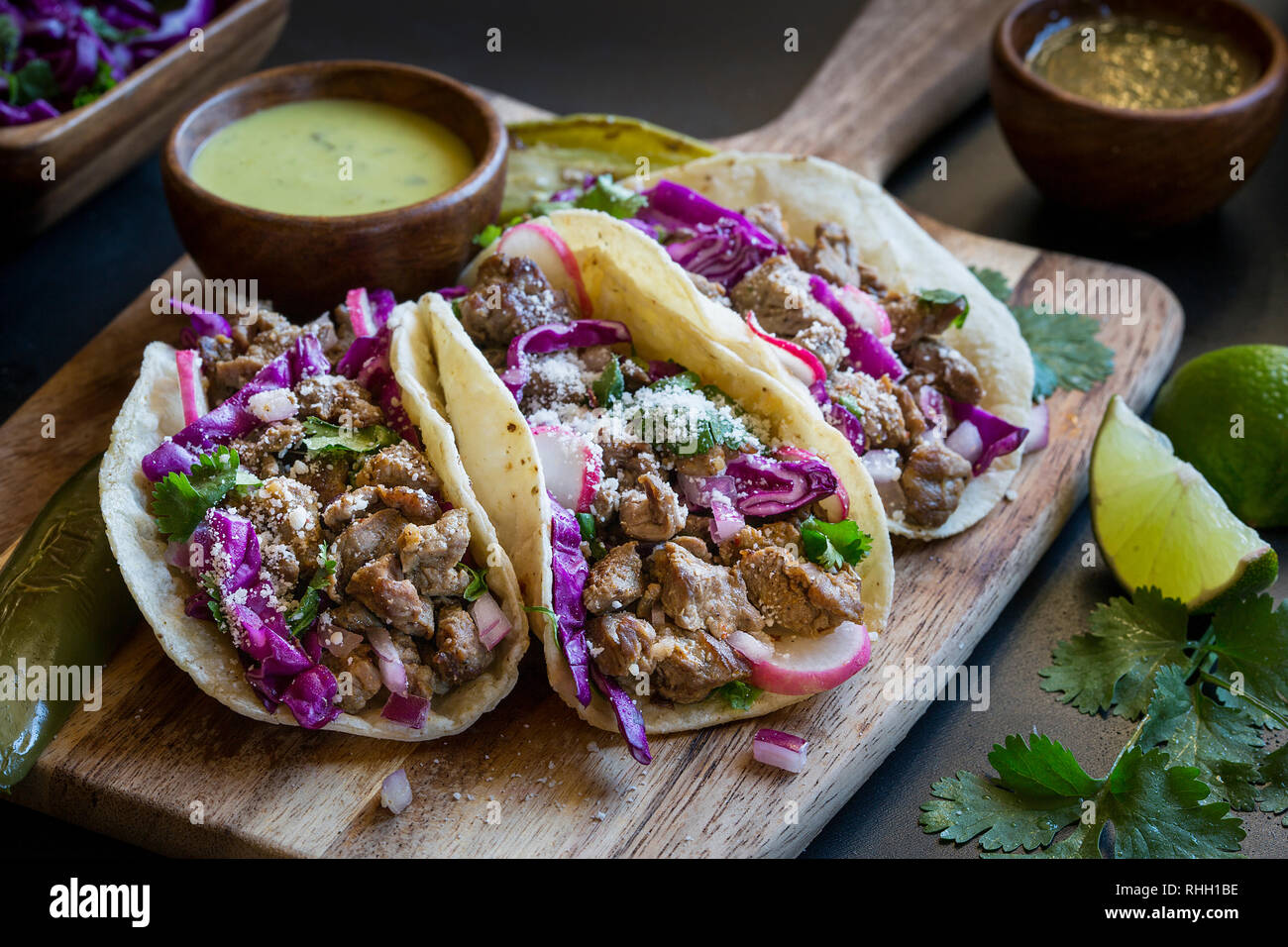 Planche de bois avec la nourriture mexicaine- 3 tacos steak violet avec le chou et le fromage cotija, servi avec de la salsa verde et de la chaux. Banque D'Images