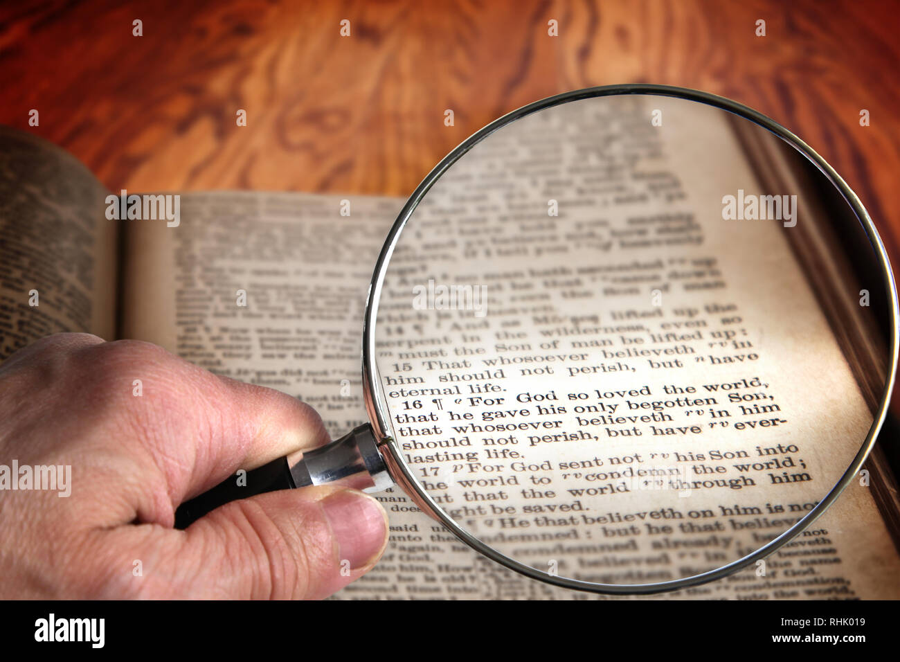 Main tenant loupe sur une vieille Bible ouverte pour le célèbre verset de Jean 3:16. Cette traduction est le roi Jacques, qui est du domaine public. Banque D'Images