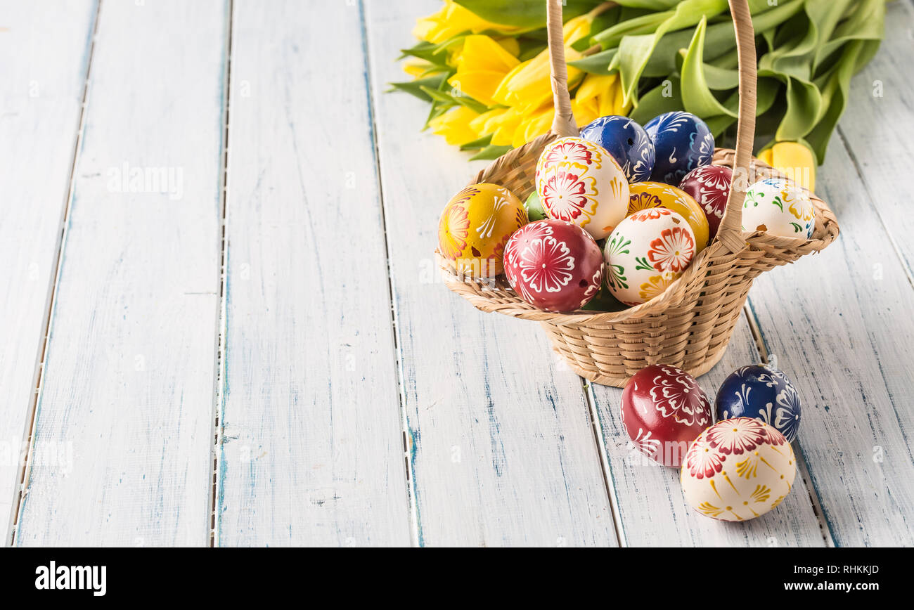 Oeufs de Pâques en panier et tulipes au printemps sur table en bois. Banque D'Images