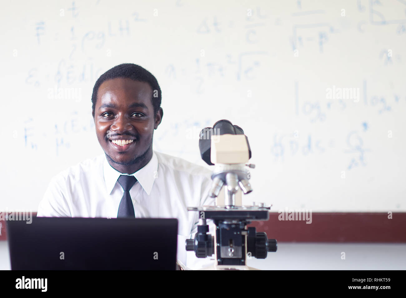Professeur de sciences de l'Afrique de l'enseignement et souriant dans la tige classe avec microscope et ordinateur. Banque D'Images