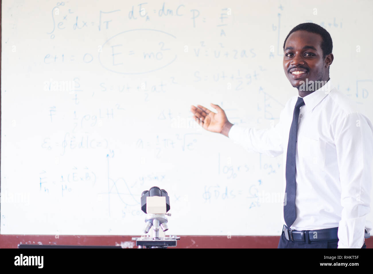 Professeur de sciences de l'Afrique de l'enseignement et souriant dans la tige classe avec microscope. Banque D'Images