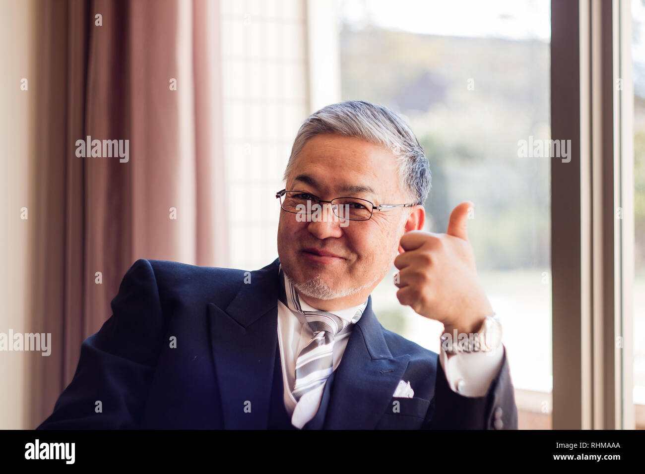 Un bel homme japonais donnant un coup de pouce à l'appareil photo en tenue de mariage formel Banque D'Images