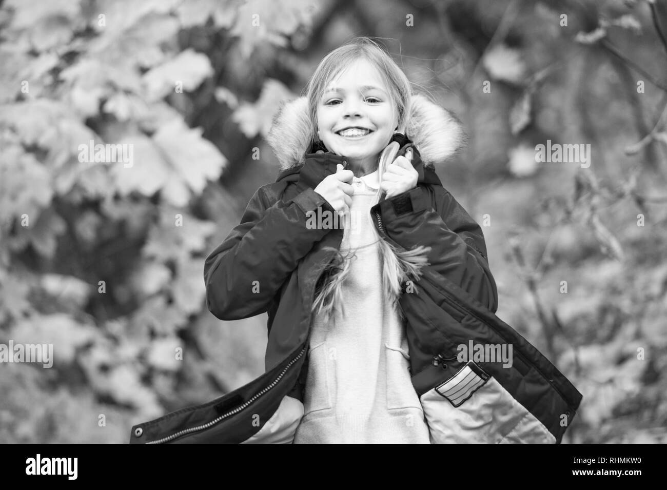 Sens tellement confortable en veste chaude. De longs cheveux blonds de l'enfant marche dans veste chaude à l'extérieur. Fille heureuse dans le parc naturel de l'automne profitez d'armoiries. L'usure de l'enfant avec capuche manteau à la mode. Vêtements d'automne et de la mode concept. Banque D'Images