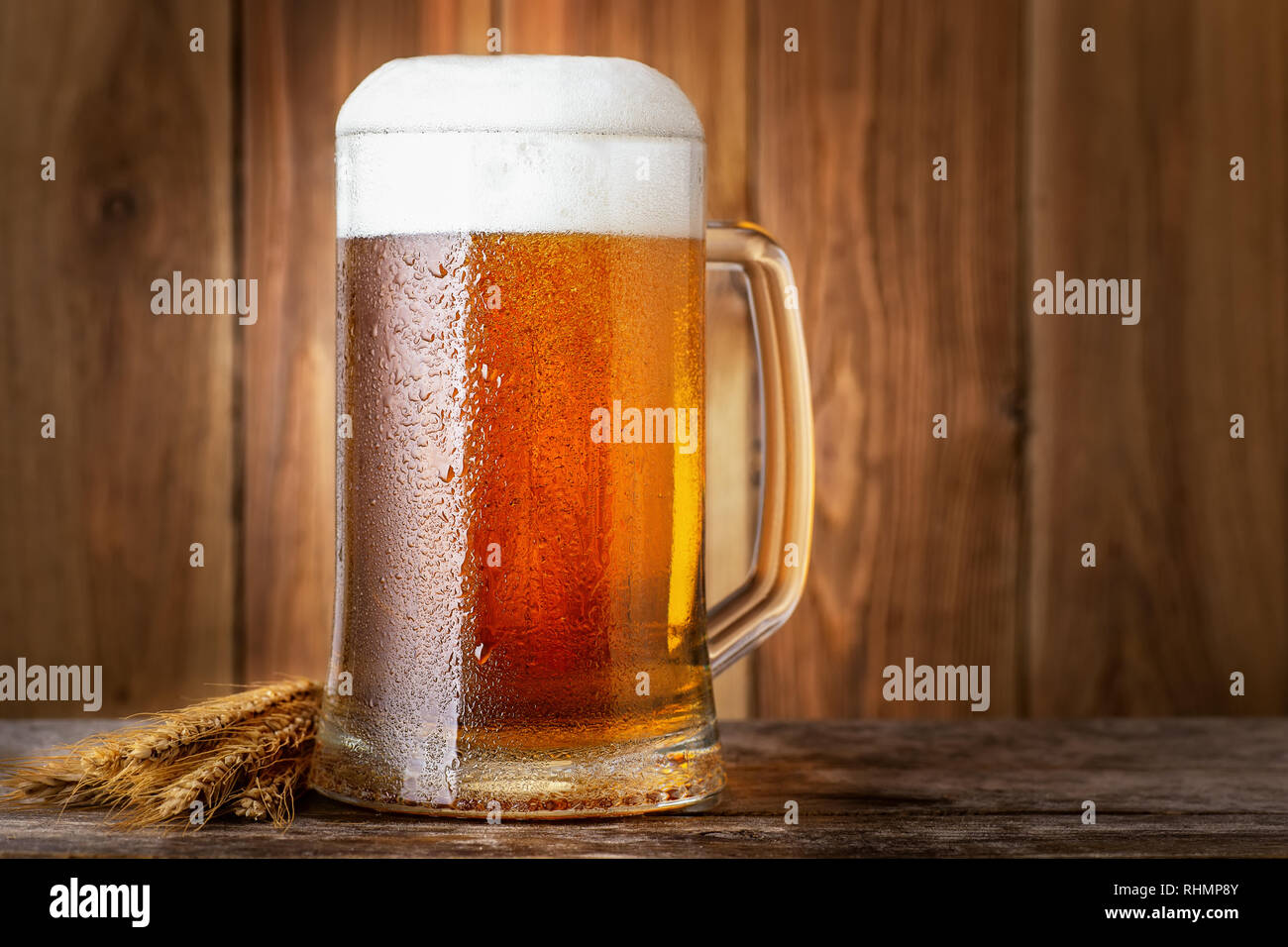 Chope de bière légère froide avec les épis de blé sur table en bois Banque D'Images