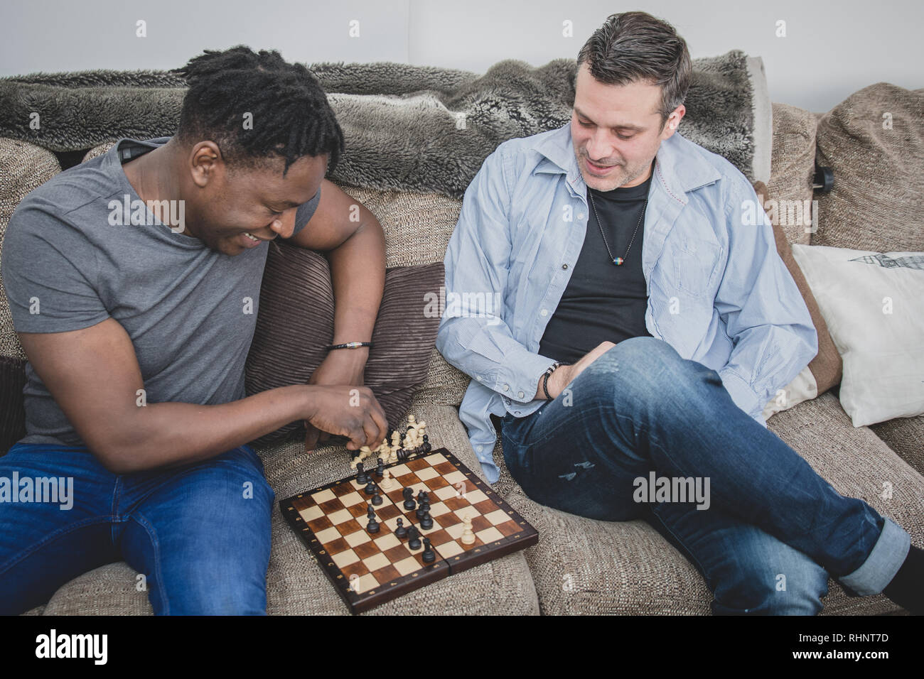 Un couple gay, bénéficiant de temps à l'intérieur à la maison, jouant aux échecs. Banque D'Images