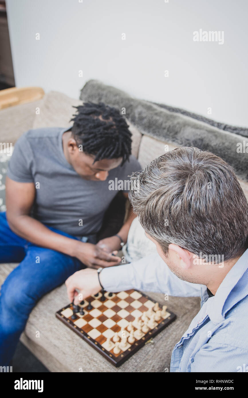 Un couple gay, bénéficiant de temps à l'intérieur à la maison, jouant aux échecs. Banque D'Images
