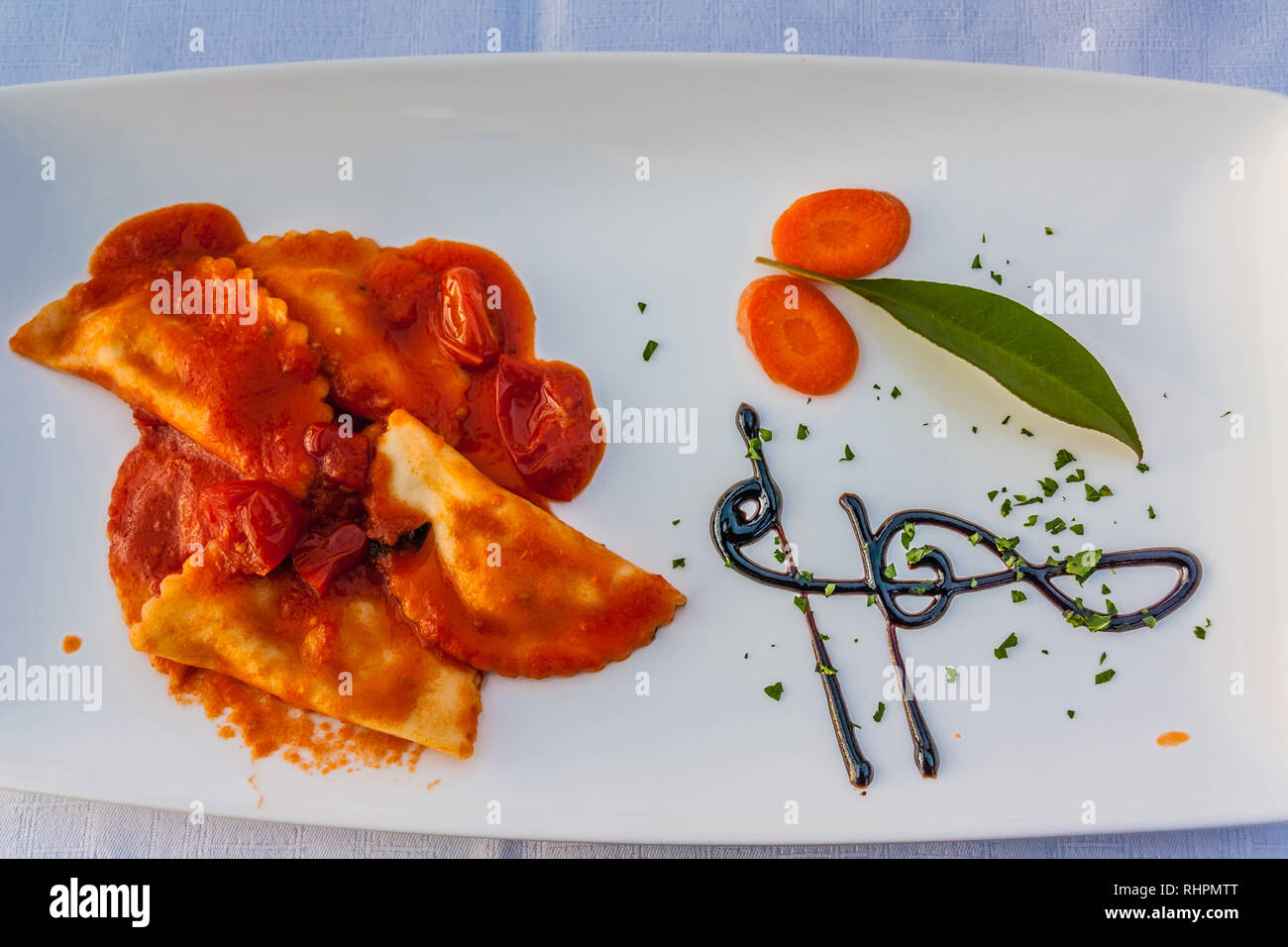 Raviolis sauce tomate sur une plaque blanche, avec une clé de sol design dans la réduction de balsamique. Banque D'Images