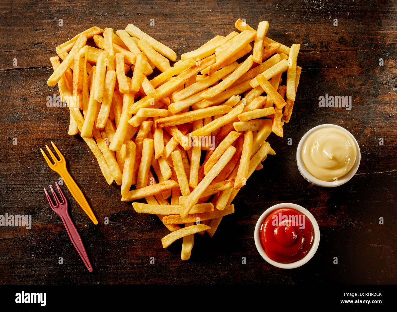 En forme d'coeur portion de frites avec des trempettes, vinaigrettes ou sauces dans de petits bols à côté sur bois Banque D'Images