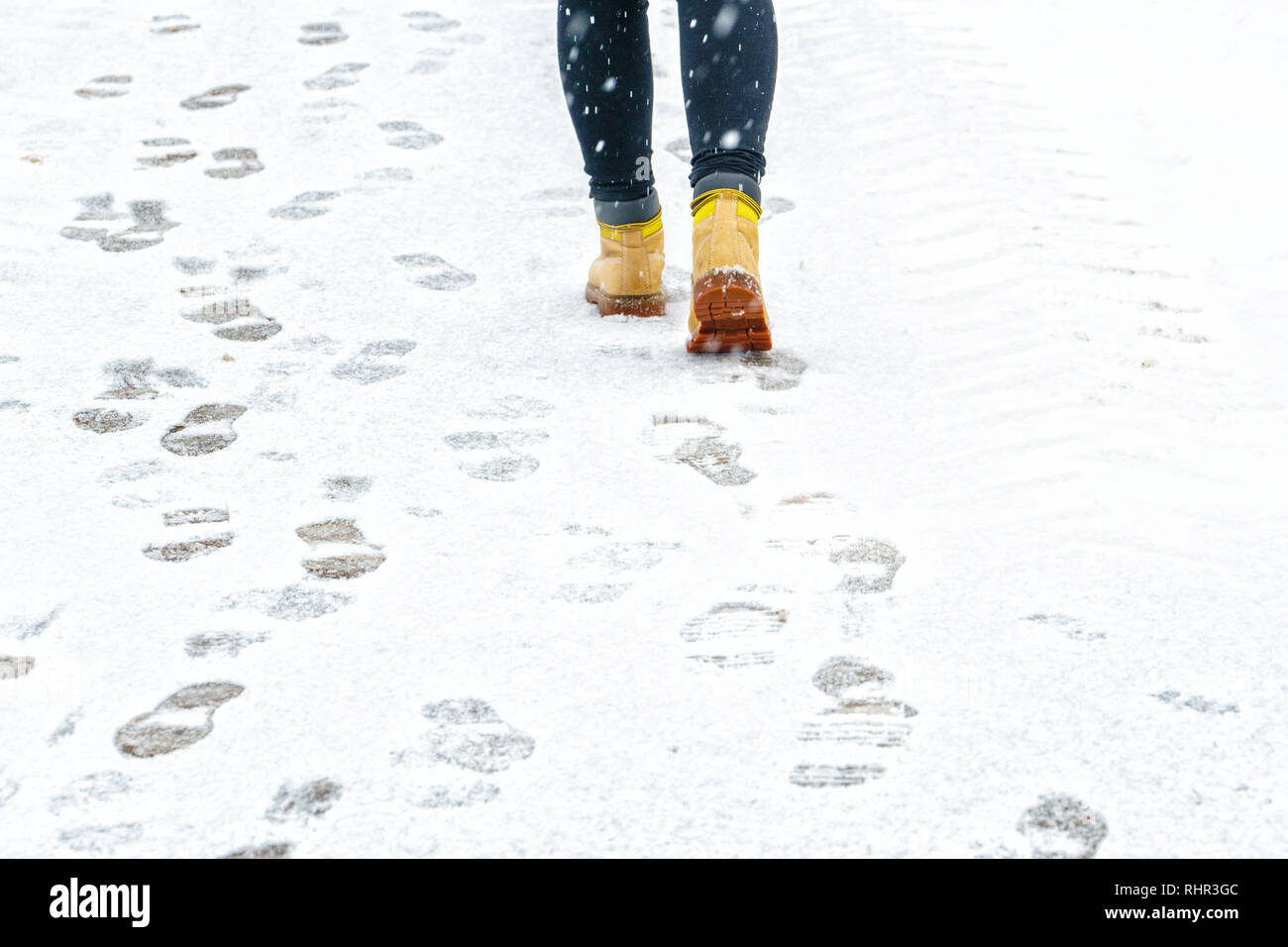 Promenade dans l'hiver Bottes en cuir jaune. Vue arrière sur les pieds d'un homme marchant le long de la chaussée enneigée glacée. Paire de chaussure sur route glacée en hiver. Abstract Banque D'Images