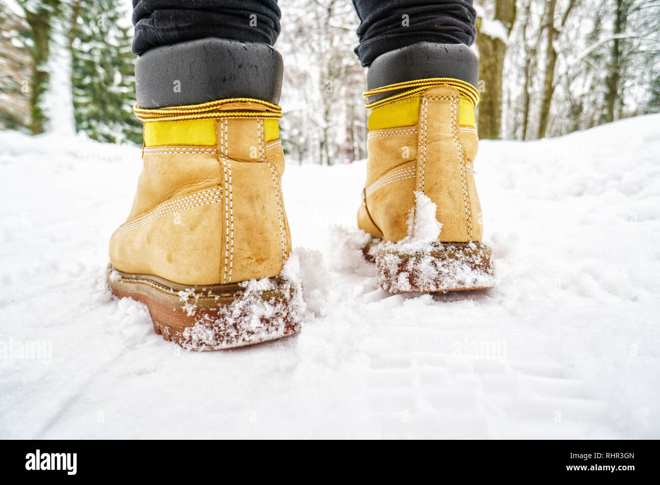 Promenade dans l'hiver Bottes en cuir jaune. Vue arrière sur les pieds d'un  homme marchant le long de la chaussée enneigée glacée. Paire de chaussure  sur route glacée en hiver. Abstract Photo