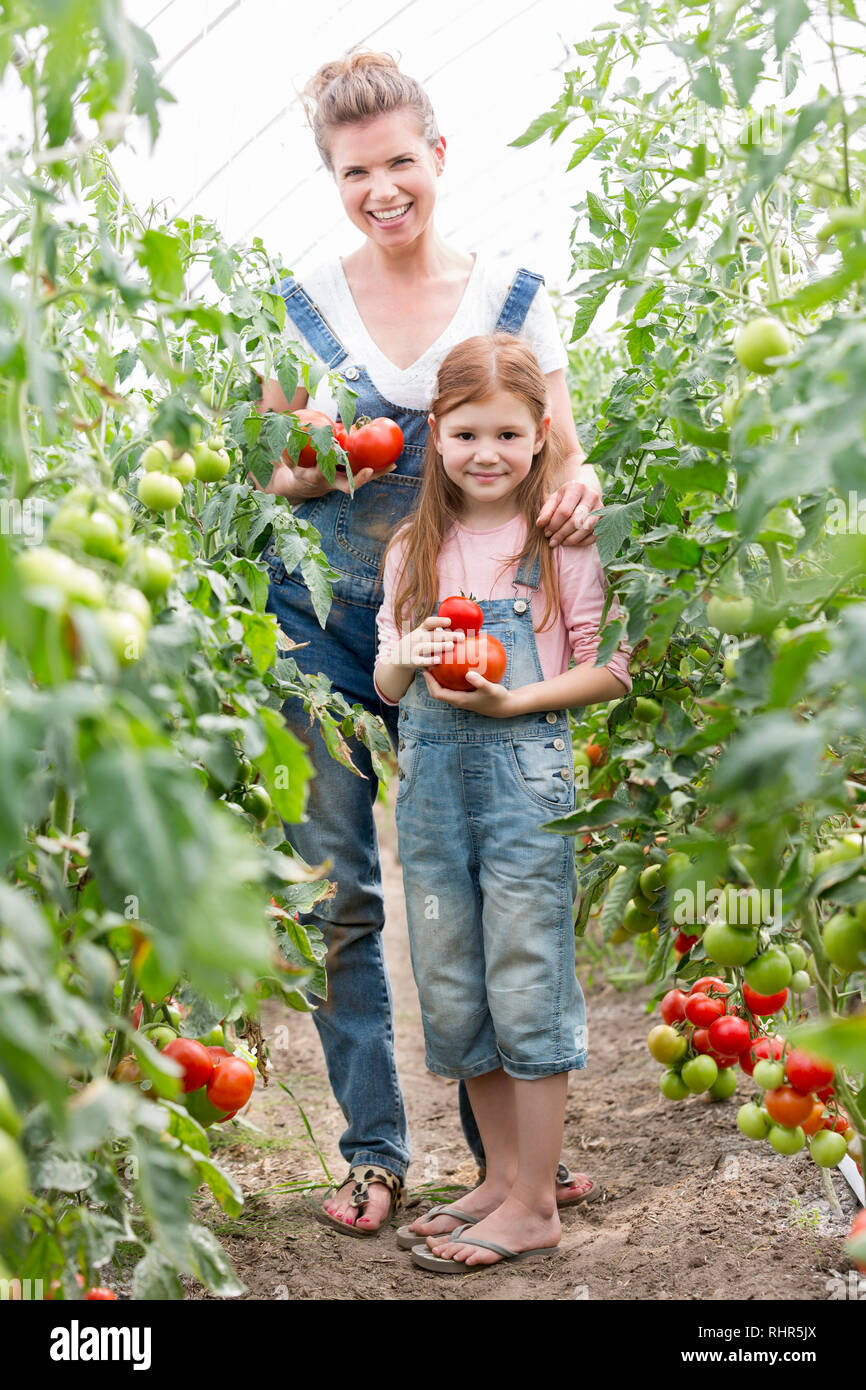 Portrait of smiling mother and daughter standing au milieu de plants de tomate à la ferme Banque D'Images