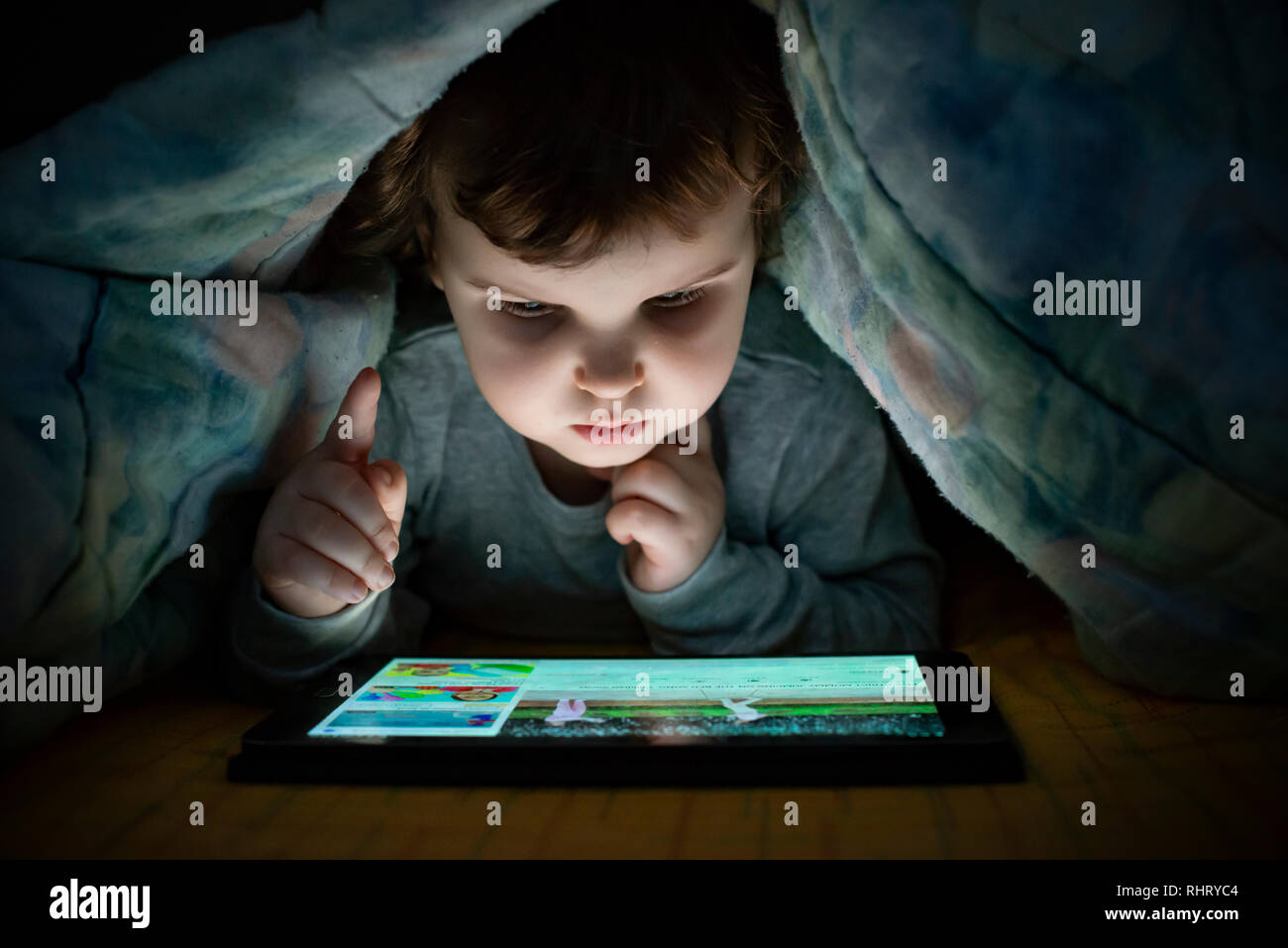 Petite fille regardant sa tablette dans le lit. Image visage d'enfants lumineux de l'écran de l'appareil. Pyjama enfant habillé avec la tenue d'une tablette. Nigh Banque D'Images