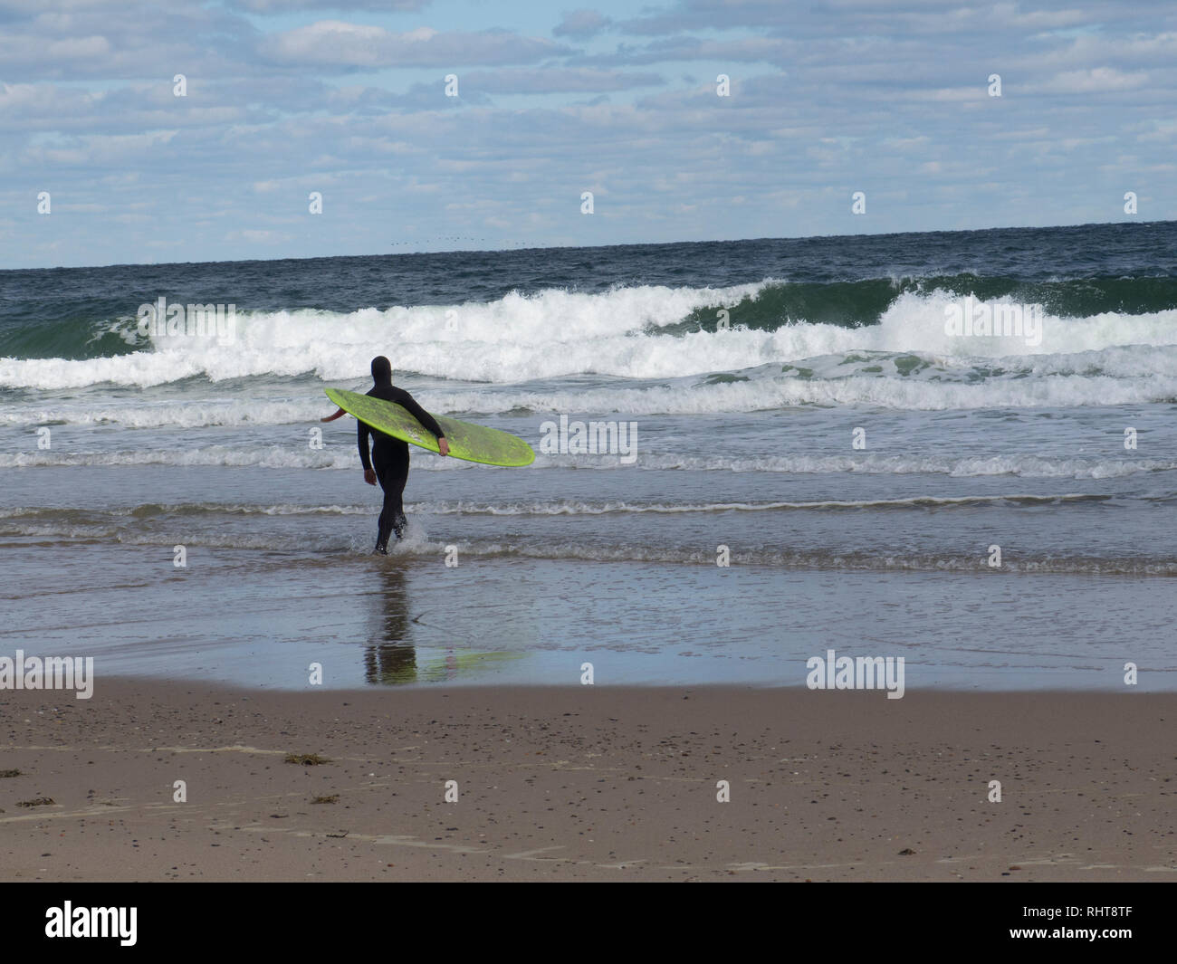 Un surfeur à Cape Cod au Massachusetts chefs pour l'eau froide dans une combinaison isothermique. Banque D'Images