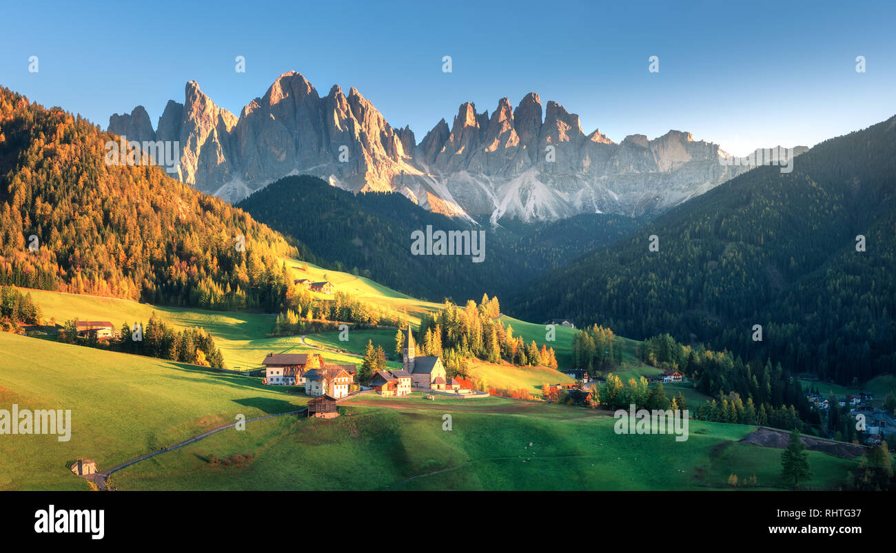 Paysage avec village avec des maisons, église, verts pâturages, arbres, roches, ciel bleu. Santa Maddalena en vallée de montagne au coucher du soleil en automne à Dolomites Banque D'Images
