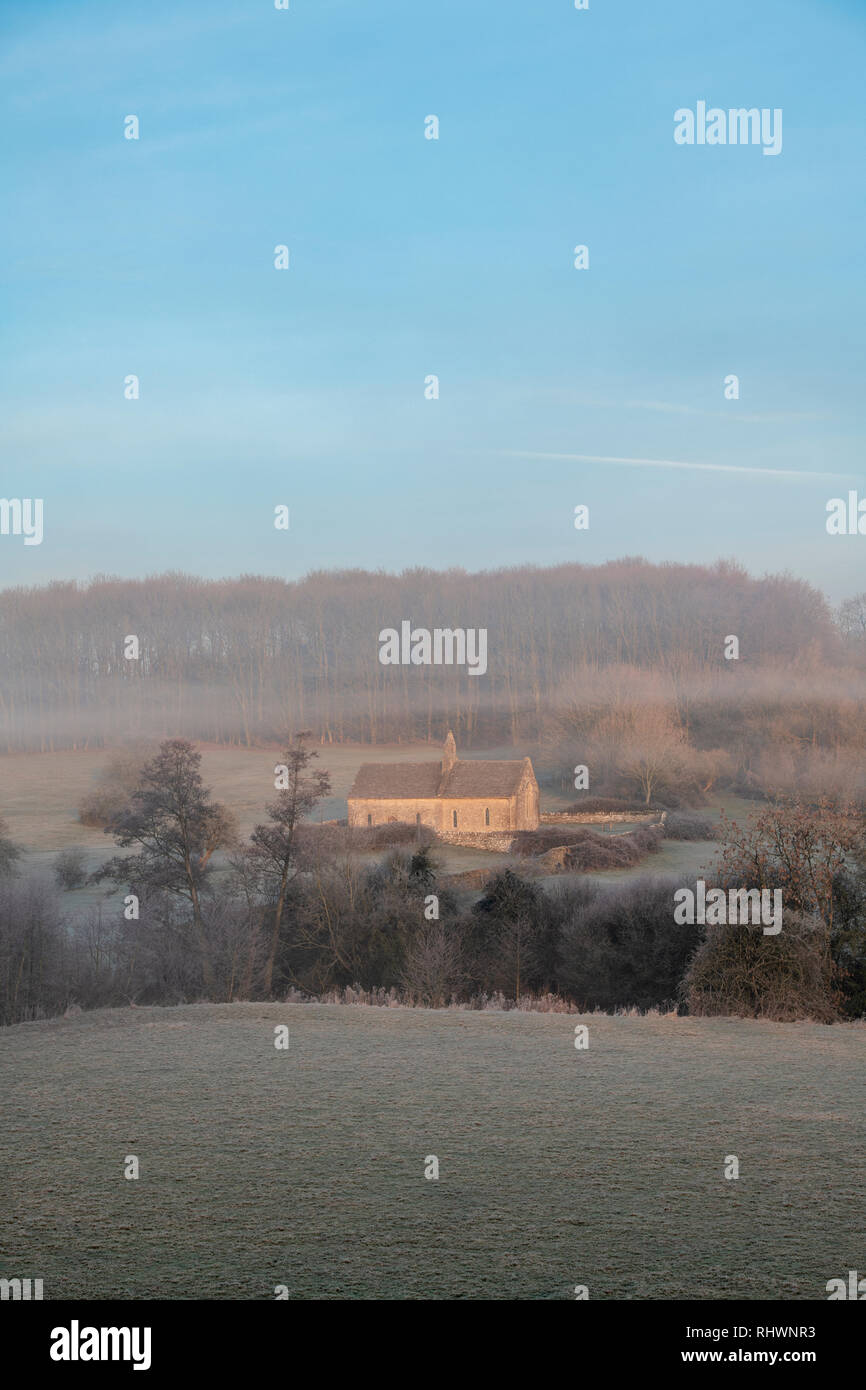 L'église St Oswald dans le brouillard d'hiver et le gel au lever du soleil. Widford, Cotswolds, Oxfordshire, Angleterre Banque D'Images