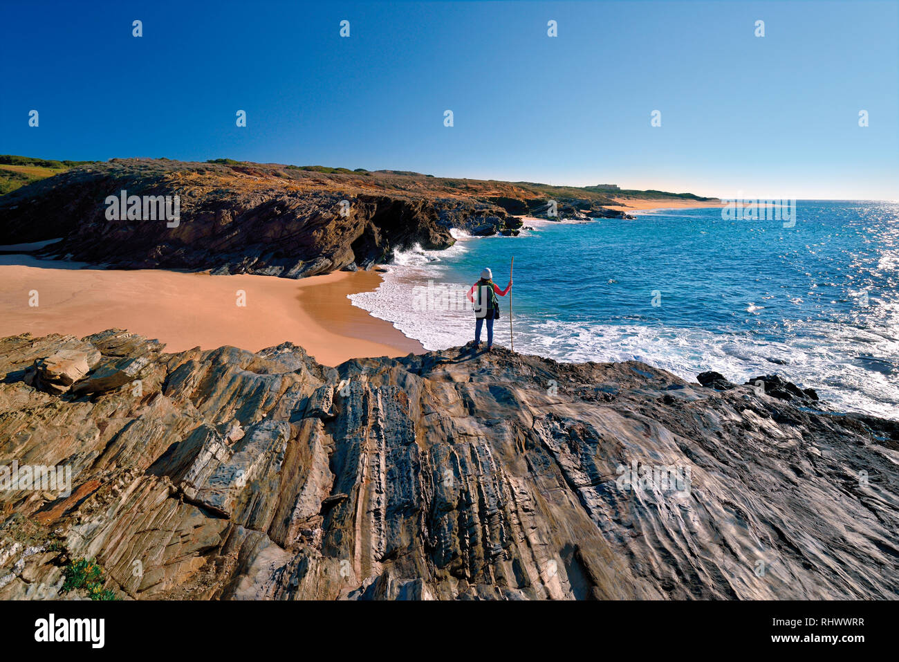 Femme avec randonnées touristiques tenue debout sur une falaise rocheuse surplombant une plage de sable sauvage Banque D'Images