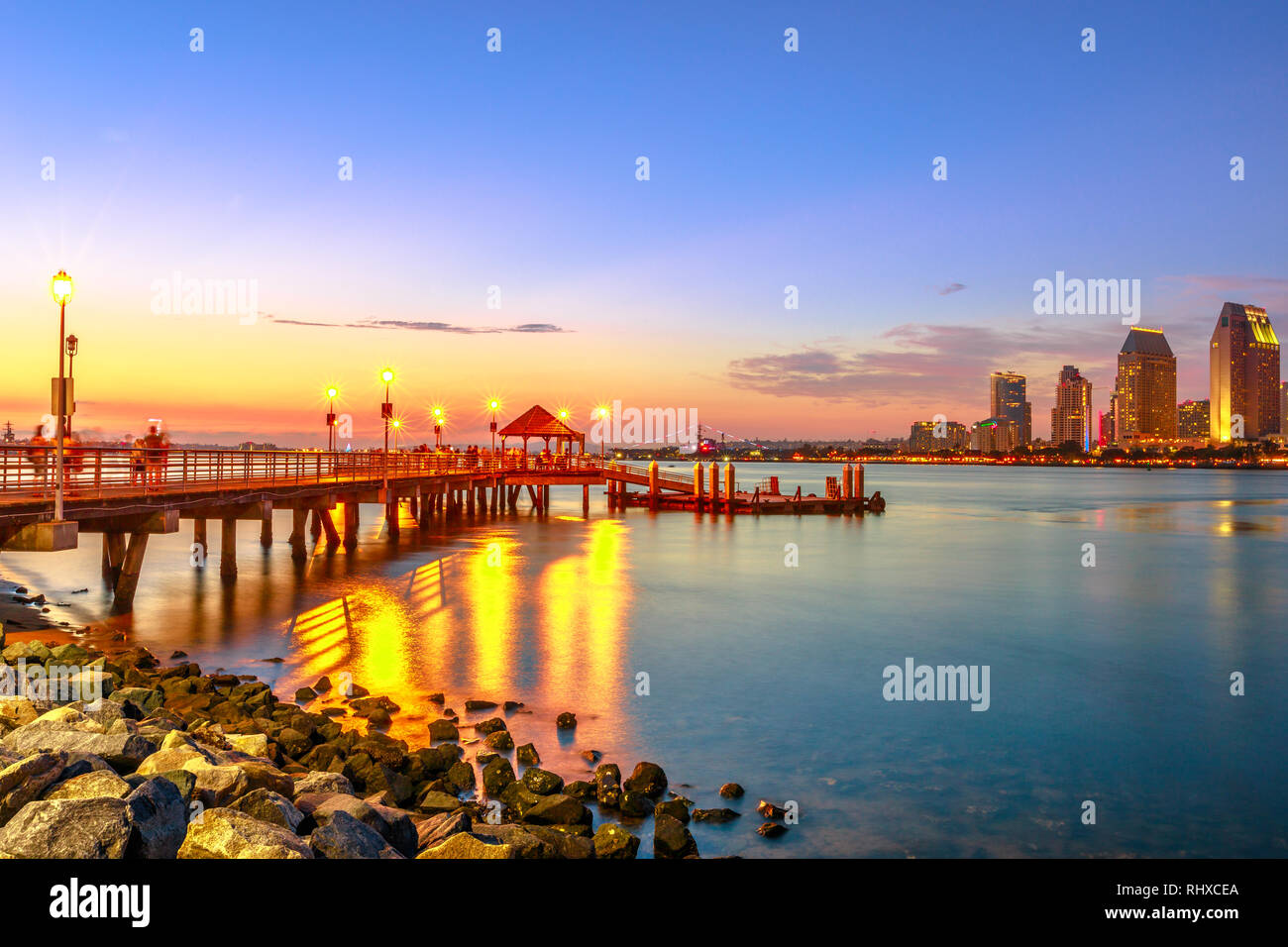 Vue panoramique de Coronado Ferry Landing sur Coronado Island, Californie, USA. Le centre-ville de San Diego au crépuscule sur l'arrière-plan. Ancienne jetée en bois reflétant Banque D'Images