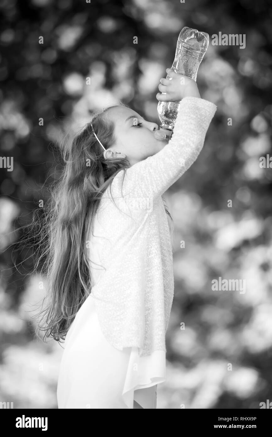 Fille soif boire l'eau de bouteille sur fond naturel. Petit enfant boire de l'eau fraîche. La soif et la déshydratation. Rafraîchissement et de fraîcheur. L'enfance et de la santé, noir et blanc. Banque D'Images