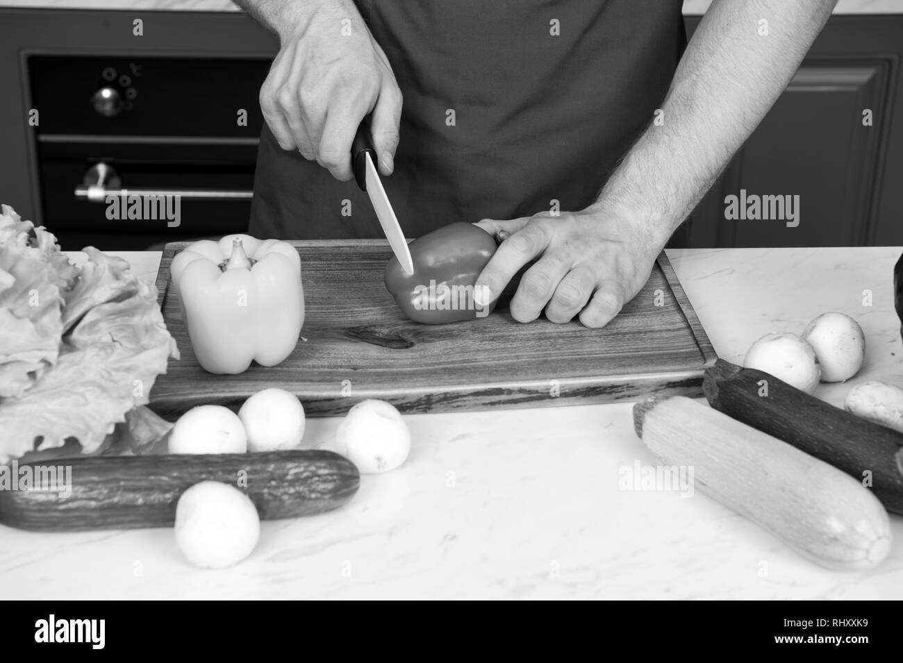 Poivron rouge coupé les mains à l'aide d'un couteau sur la planche à découper en bois. Légumes, salade concombre courge, champignons vitamine. Végétarien, régime alimentaire santé concept. Alimentation, la cuisine de préparation. Banque D'Images
