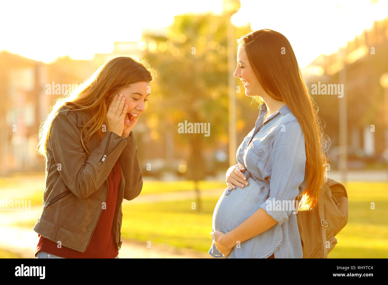 Surpris girl looking at son ami enceinte ventre dans un parc au coucher du soleil Banque D'Images