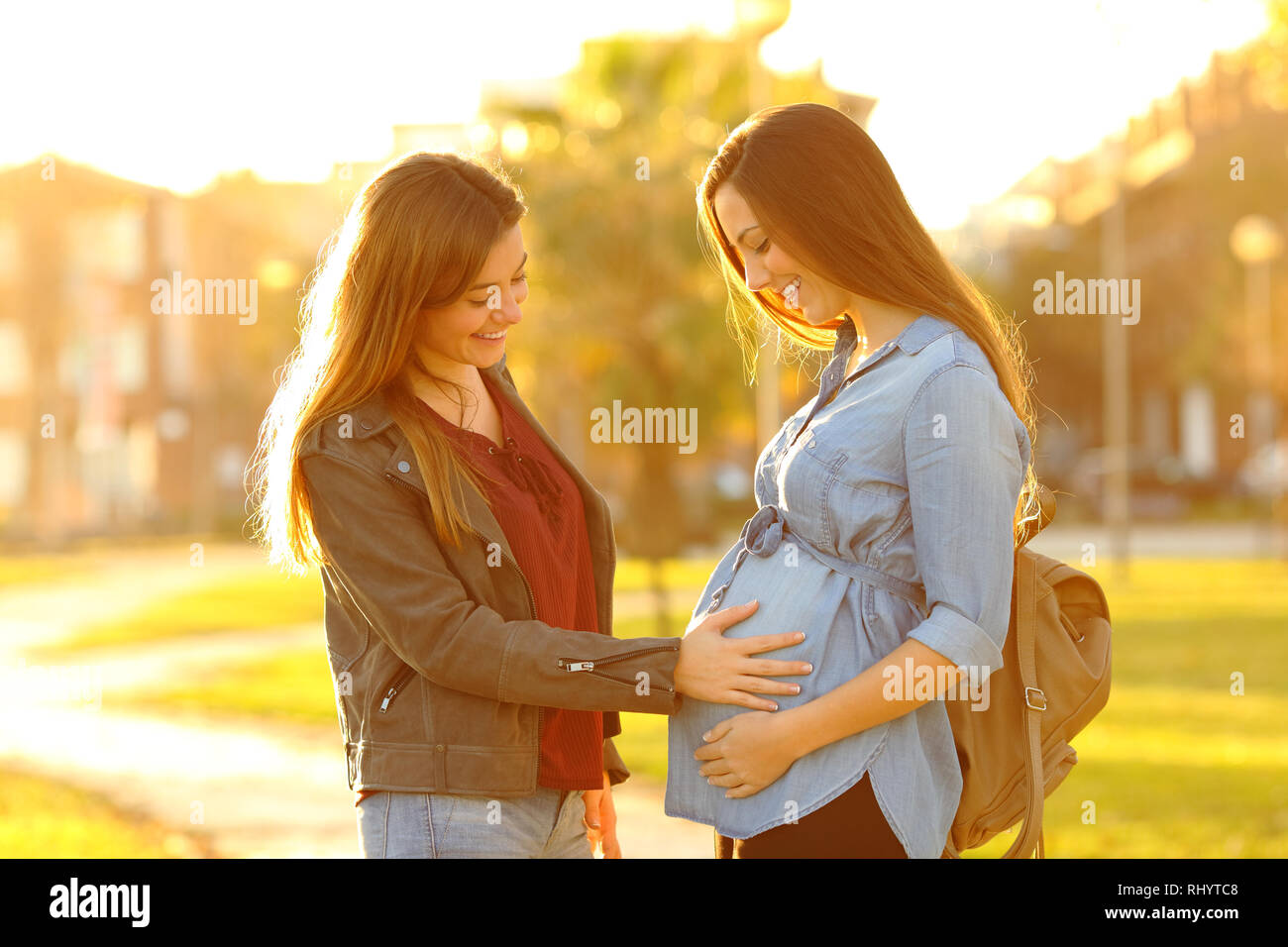 Happy pregnant woman showing ventre à un ami dans un parc au coucher du soleil Banque D'Images