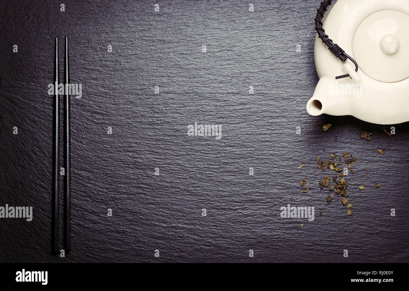 La composition des aliments en Asie avec des baguettes chinoises, théière et sèche thé vert sur une pierre sombre arrière-plan, Vue de dessus, tonique, avec de l'espace libre pour le texte Banque D'Images