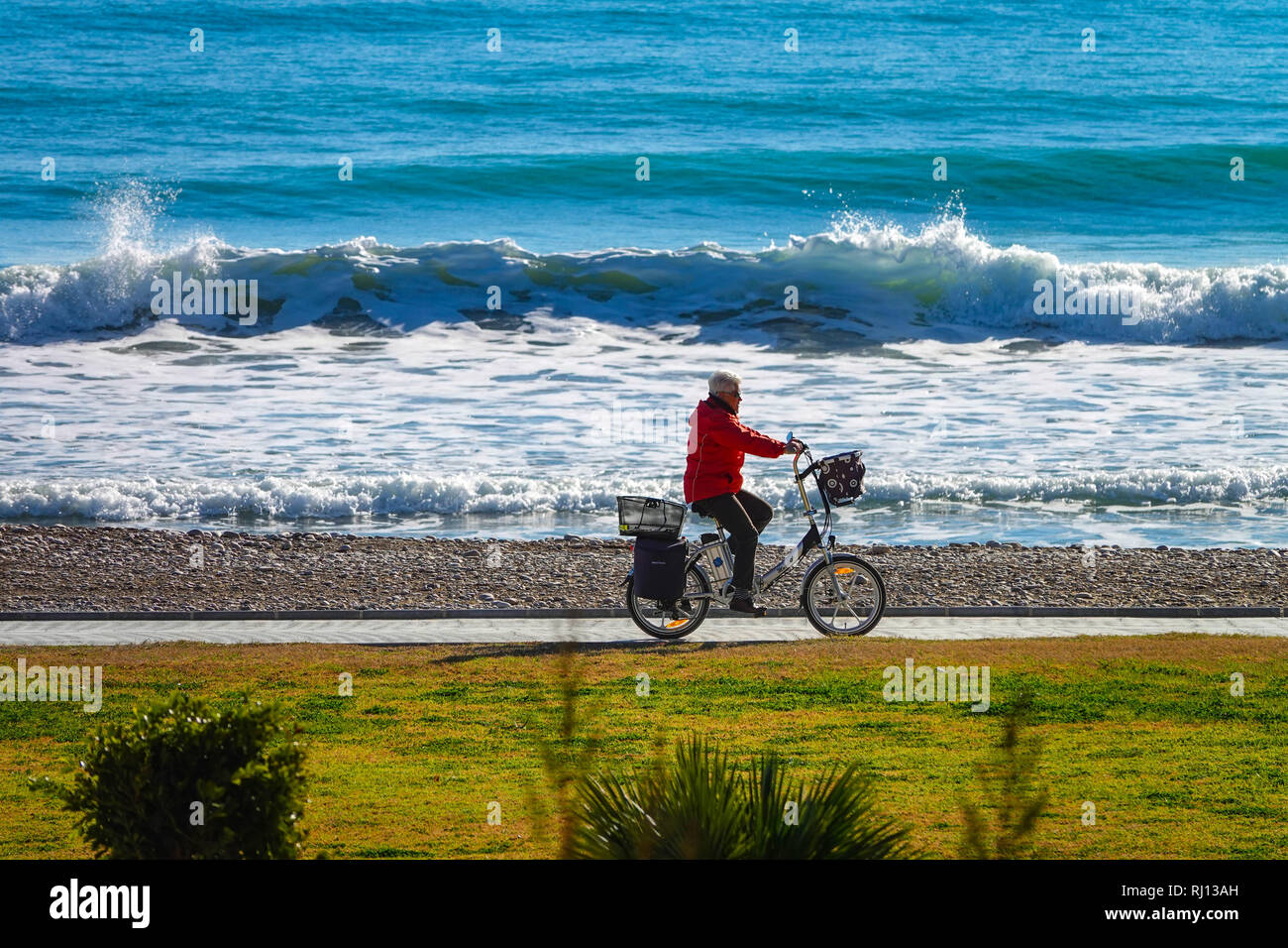 Personne plus âgée à vélo avec vélo électrique, la Promenade et la mer avec des vagues à Oropesa del Mar, Costa del Azahar, Province Castellon, Espagne, Oropesa Banque D'Images