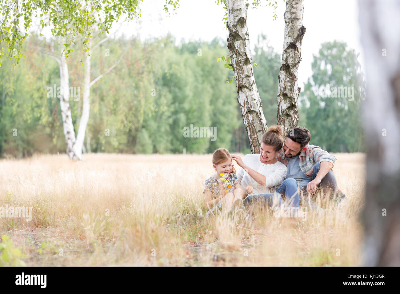 Les parents assis avec sa fille contre l'arbre sur les terres agricoles au champ Banque D'Images