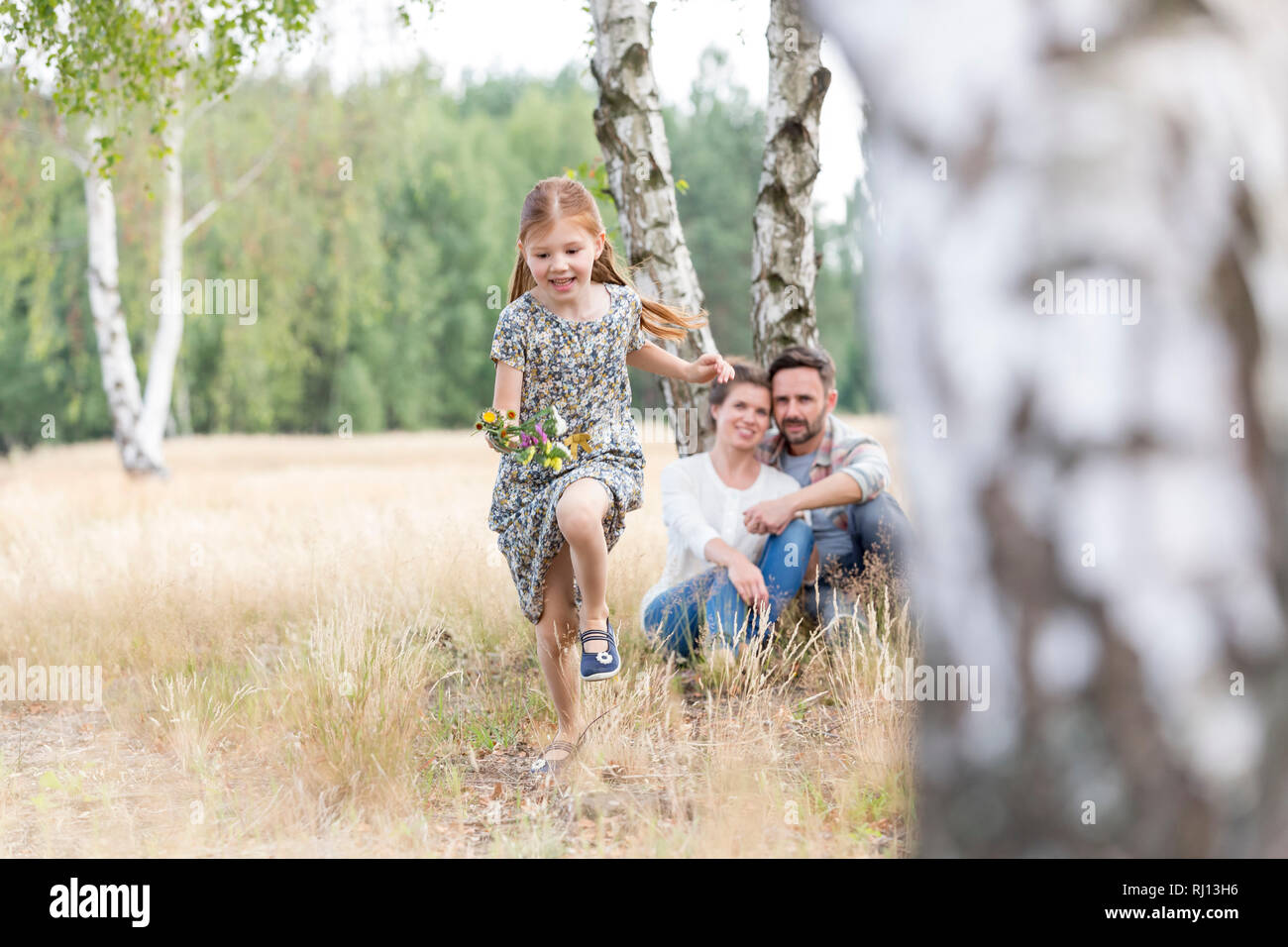 Fille courir sur terrain tandis que les parents assis à terre agricole Banque D'Images