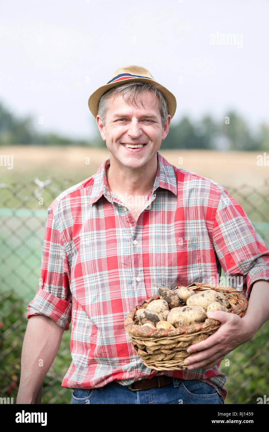 Portrait of smiling farmer transportant des pommes de terre biologiques dans panier à la ferme Banque D'Images