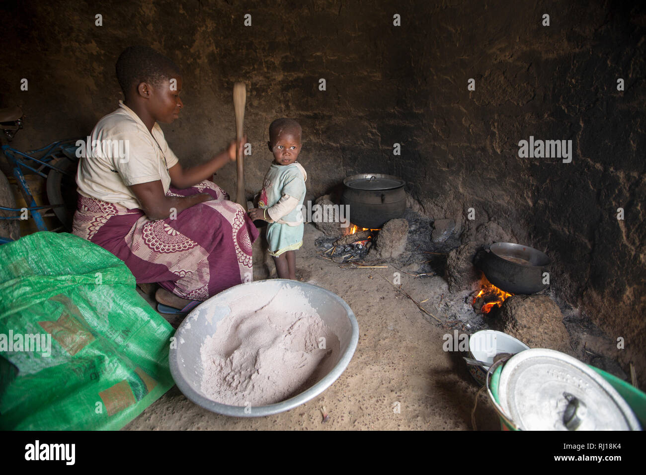 Village de samba, Province de Yako, Burkina Faso : Collette Guiguemde, 26 avec son bébé et de ses quatre ans, fille de livres chili pour aller avec un repas de gombo qu'elle vient de récolter et de sorgho du porridge. Banque D'Images