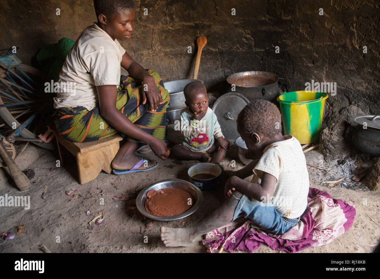 Village de samba, Province de Yako, Burkina Faso : Collette Guiguemde, 26 avec son bébé et sa fille au repas de gombo qu'elle vient de récolter et de sorgho du porridge. Banque D'Images