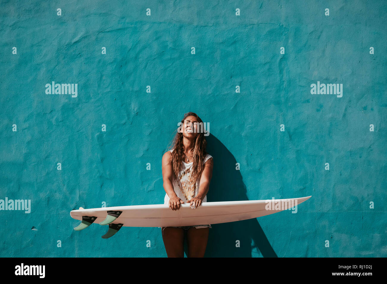 Heureux Surfer Girl with surfboard en face du mur bleu Banque D'Images