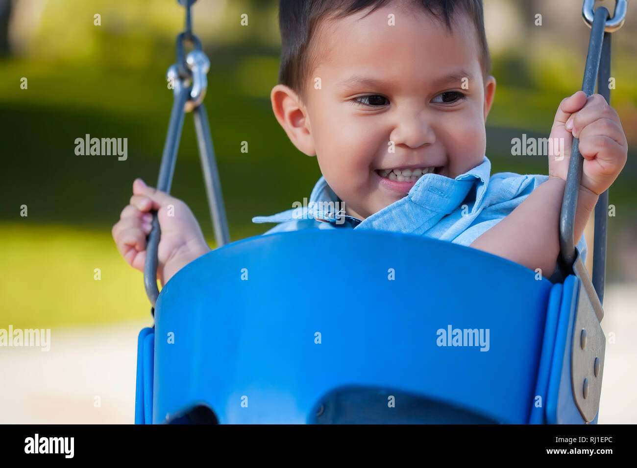 Young hispanic boy avec un sourire mignon qui est à la recherche, tandis que l'équitation et la tenue à une aire de swing. Banque D'Images