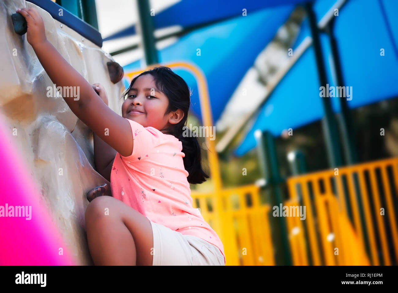 A smiling pre teen girl looking down alors qu'elle atteint le sommet d'un mur d'escalade salle de sport. Banque D'Images