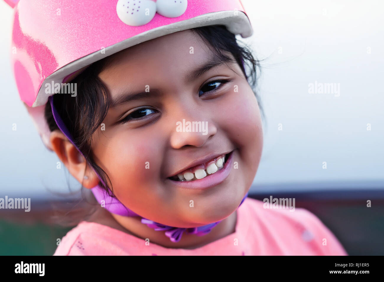Smiling pre teen kid pluriethniques, avec un ensemble complet des dents et le port d'un casque de vélo rose. Banque D'Images