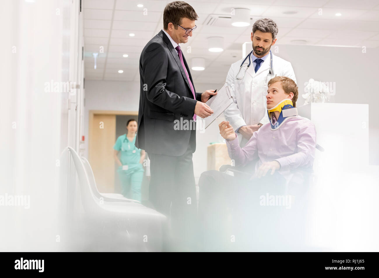 Spécialiste mature talking to patient sur fauteuil roulant à l'hôpital Banque D'Images