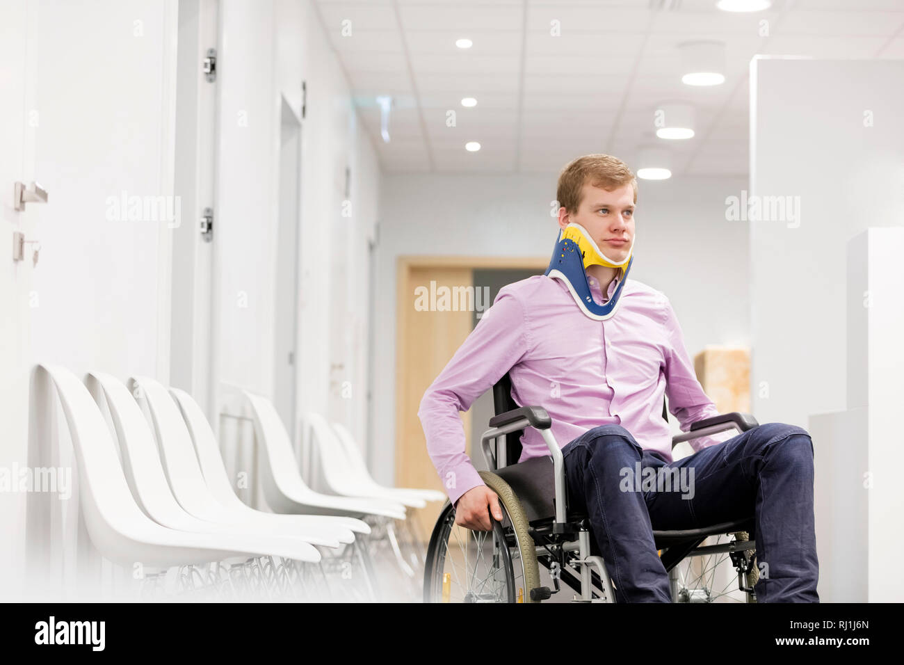 Jeune homme avec neck brace assis sur fauteuil roulant à hospital corridor Banque D'Images