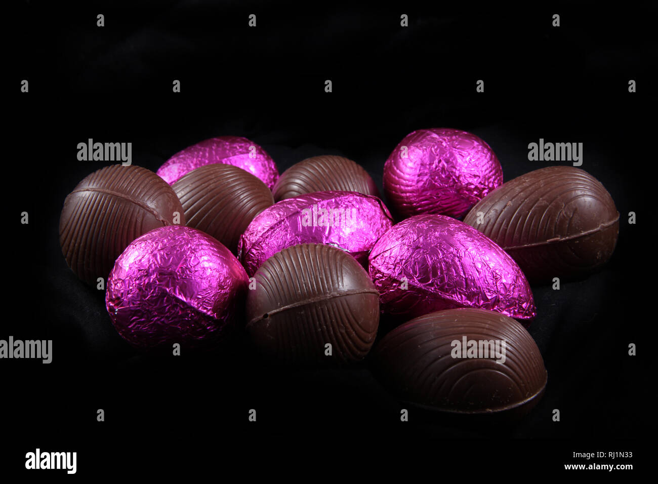 Pile de papier aluminium rose enveloppé & unwrapped chocolate Easter eggs sur fond noir. Banque D'Images