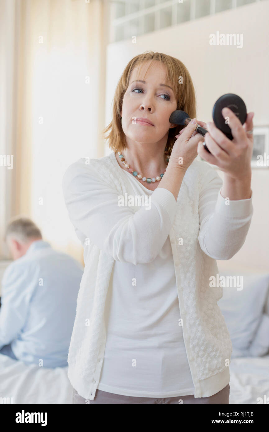 Young woman applying makeup tout en se tenant dans la chambre Banque D'Images